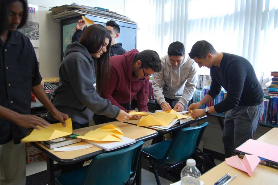 Economics students follow Henry Fords assembly line methods to construct paper airplanes. 
