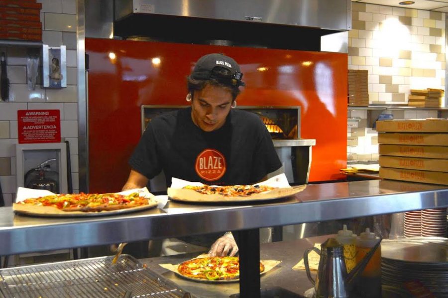 A worker cuts the pizza that just came out of the oven. After choosing the toppings you want on your pizza, the pizza is put into a large oven. The workers are very efficient and serve you quickly.