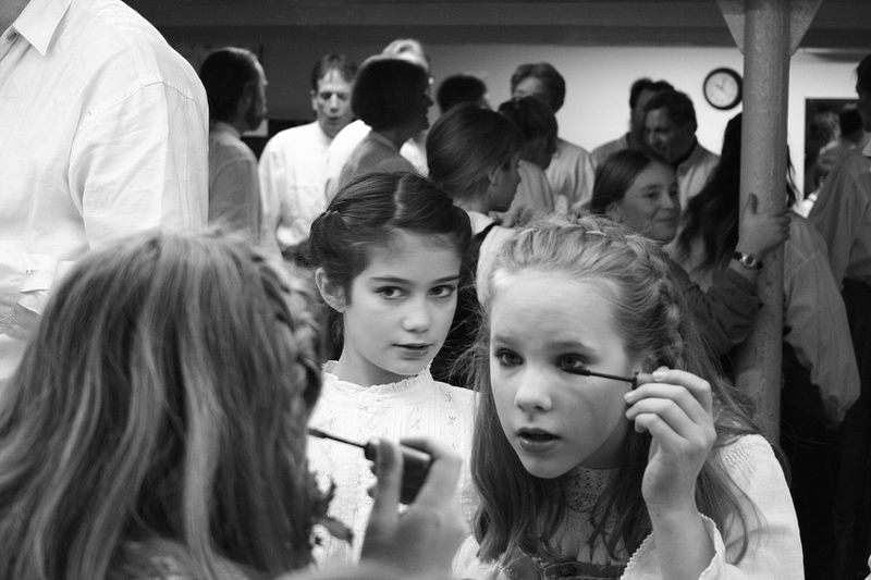 A picture showing a young girl applying makeup and her friend thinking whether she should do the same or not.  