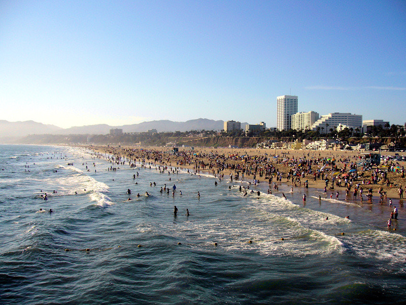 Friends and families enjoy swimming and surfing on a sunny day at Santa Monica beach.