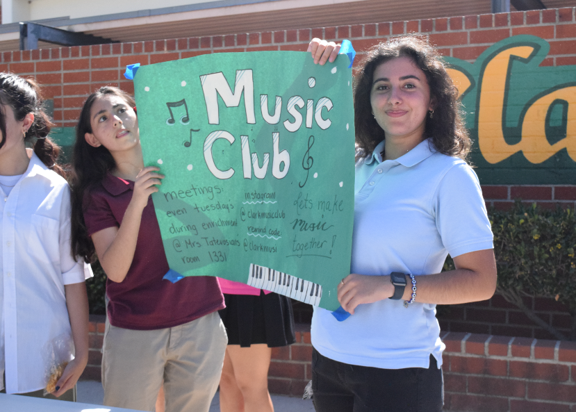 Students representing music club proudly hold up a sign. 
