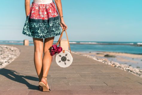 Girl walking alongside the beach with raffia handbag and straw sandals.