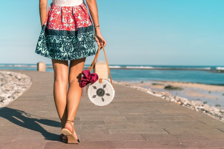 Girl+walking+alongside+the+beach+with+raffia+handbag+and+straw+sandals.