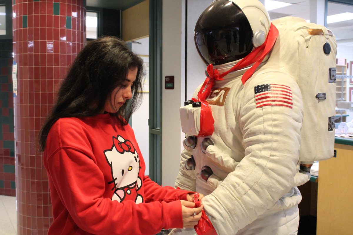 Senior KATS Club secretary Camila Cancik ties a red ribbon around the arms of the astronaut during Red Ribbon Week. 