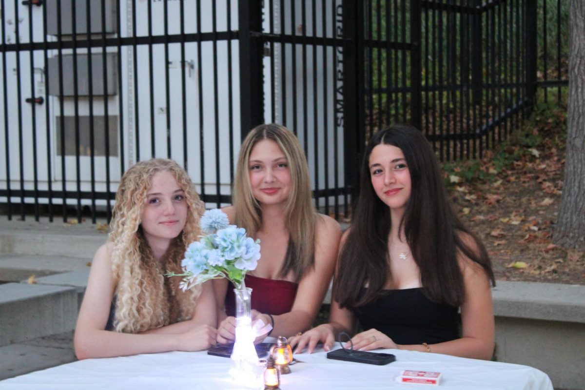 Seniors Evlana Panelli, Amarise Fisher, and  Aline Melconian sitting at one of the tables which were used for studying and eating a few hours ago, but have now been turned into elegantly decorated tables for guests at Homecoming.
