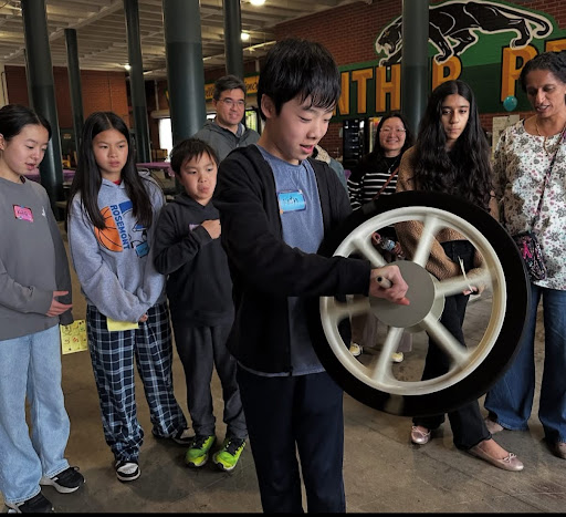 A student experiences the force of torque by holding a wheel and stepping on a rotating platform. 