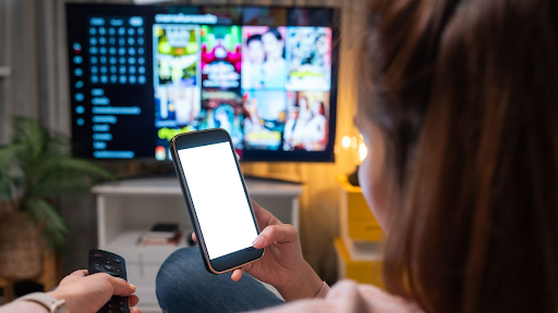 A woman is on her phone while Netflix is on the TV in the background.